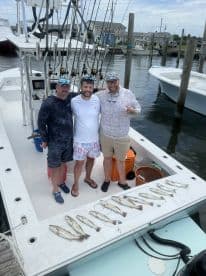 Three anglers proudly displaying their catch of Speckled Trout on the deck of a fishing boat after a successful outing.