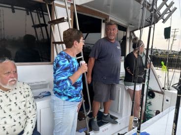 A group of anglers aboard a fishing charter boat, preparing for their trip. The interior features multiple fishing rods and a relaxed atmosphere.