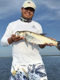 Angler proudly displaying a large Tarpon while fishing in a scenic coastal environment.