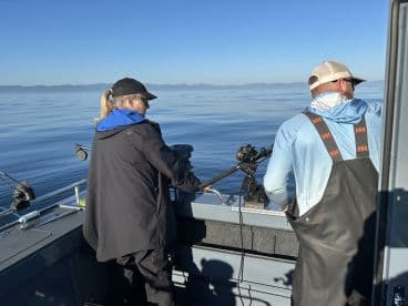 Two anglers actively fishing on a calm day, with clear blue skies and a serene water backdrop.