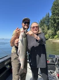 Two anglers proudly displaying a large Salmon on a fishing boat, enjoying a sunny day on the water.