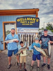 A family proudly displaying their catch of Lake Huron fish, including multiple Walleye, in front of Wellman's Party & Bait in Oscoda, MI.
