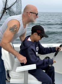A young angler is being guided by an adult while reeling in a fish on a boat, showcasing an engaging fishing experience on the open water.