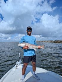 Angler proudly displaying a large Redfish on the bow of a boat in a coastal fishing environment.