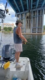 A young angler casting a line under a bridge while fishing in a calm waterway, showcasing a relaxed fishing environment.