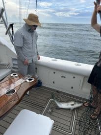A striped bass is laid out on the deck of a fishing boat, with anglers preparing for the next catch during a coastal fishing trip.