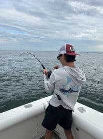 A young angler is actively reeling in a fish while fishing from a boat, showcasing the excitement of deep-sea fishing.