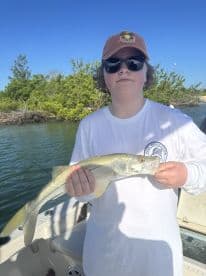 Young angler holding a Snook while fishing on a sunny day, showcasing a successful catch from a boat.