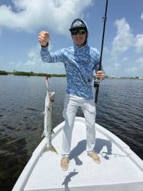 An angler proudly displaying a Barracuda while fishing from a small boat in a coastal waterway.