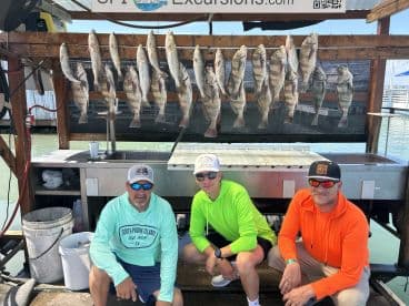 A group of anglers posing in front of a catch board displaying several Speckled Trout after a successful fishing trip in South Padre Island, Texas.