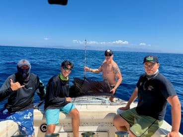 A group of anglers proudly displaying a large Sailfish on a sport fishing boat, enjoying a sunny day on the open ocean.