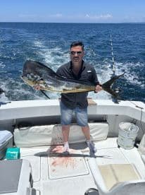 An angler proudly displaying a large Mahi Mahi on a fishing boat, showcasing a successful offshore fishing trip.