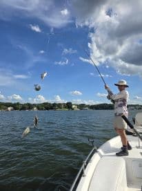 A young angler reeling in multiple fish while fishing from a boat on a sunny day, showcasing an exciting catch in a freshwater environment.
