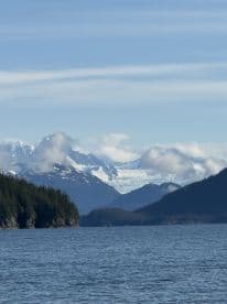 Scenic view of a glacier and mountainous landscape from the side of a fishing boat in a tranquil Alaskan waterway.