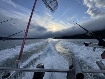 A scenic view from the boat during a fishing trip, showcasing fishing rods in action against a backdrop of a stunning sunset over the water.