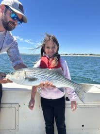 A young girl proudly displaying a striped bass while fishing on a boat, enjoying a sunny day on the water.