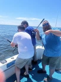 Group of anglers actively fishing on a boat, with one enthusiastically celebrating while another reels in a catch on a sunny day.