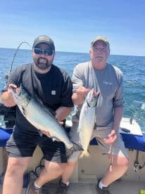 Two anglers proudly displaying their catch of Salmon while fishing on a boat in open water.