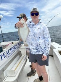 A young angler proudly displaying a Flounder while fishing aboard the 'Teacher's Pet' charter boat in a coastal setting.