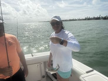 A woman proudly displaying her catch while fishing on a boat, with a sunny backdrop and calm waters.