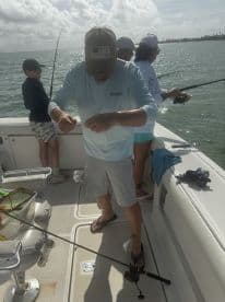 A group of anglers actively fishing on a boat, with a young boy observing as an adult prepares the line. The sunny day highlights the vibrant fishing environment.