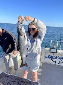An excited angler proudly displays a large Salmon aboard a fishing charter, showcasing a successful day on the water.