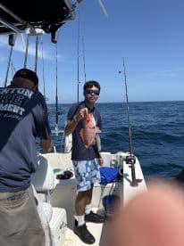 A young angler proudly displaying a Red Snapper on a fishing boat, enjoying a sunny day on the water.