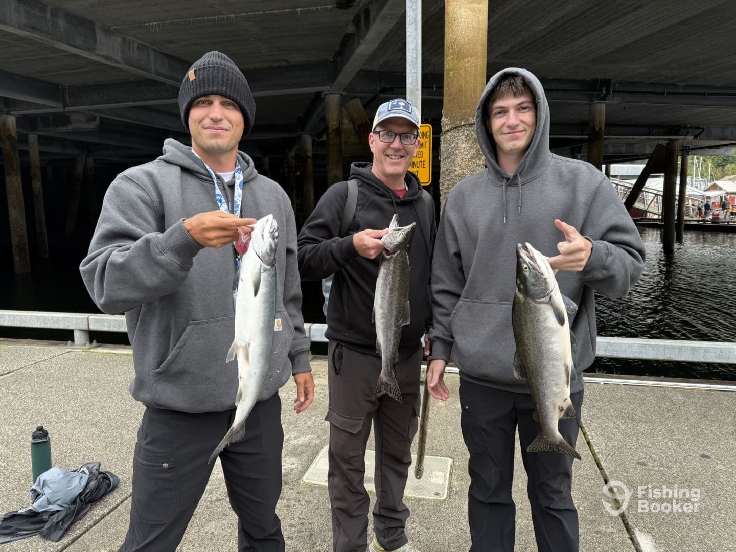 Three anglers proudly displaying their catch of Salmon at a dock, showcasing a successful fishing trip.