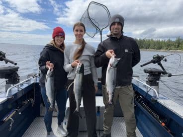 Three anglers proudly displaying their catch of Salmon while fishing on a boat in a scenic lake environment.
