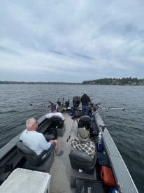 A group of anglers relaxing in the seating area of a fishing boat, equipped with multiple fishing rods, while enjoying a day on the water.