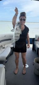 An angler proudly displaying a large Black Drum while fishing on a boat in a calm waterway.