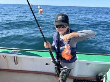 A young angler proudly displaying a colorful Red Snapper while fishing on a boat in clear blue waters.