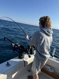 A young angler reeling in a catch while fishing on a boat in open waters, showcasing the excitement of the fishing experience.