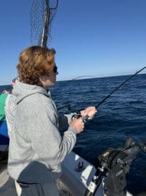 A young angler is actively reeling in a fish while fishing on a boat in open waters, showcasing the excitement of the sport.