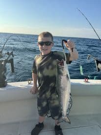 A young angler proudly displaying a large fish while fishing offshore, showcasing a sunny day on the water.