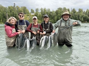 A group of anglers proudly displaying their catch of salmon while wading in a river, showcasing a successful fishing trip.
