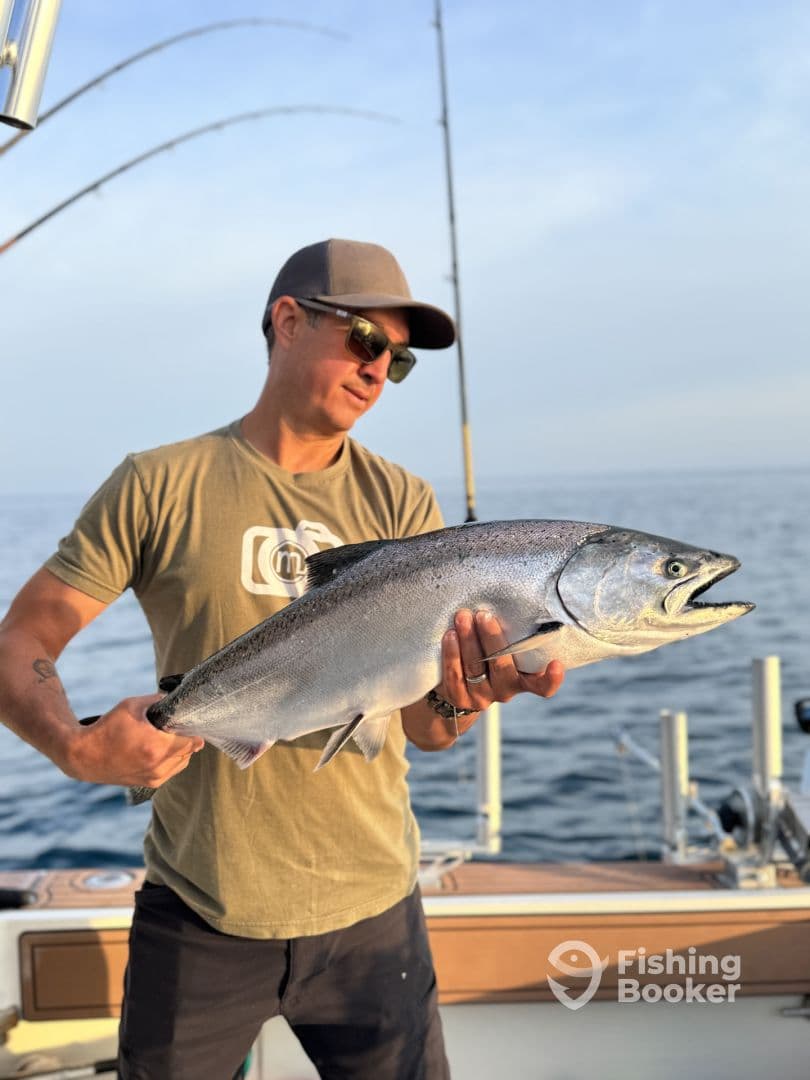 Angler displaying a large Salmon while fishing on a boat, showcasing a successful catch in a serene ocean setting.