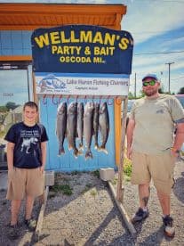 A young angler and an adult proudly pose beside a catch of Lake Huron trout displayed on a board at Wellman's Party & Bait in Oscoda, MI.