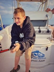 A young angler focused on reeling in a catch aboard a fishing boat, showcasing the excitement of fishing in open waters.