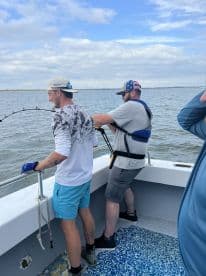 Two anglers actively reeling in a catch while fishing from a boat in a coastal waterway.