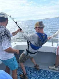 Two anglers actively reeling in a catch aboard a fishing boat, showcasing the excitement of deep-sea fishing.
