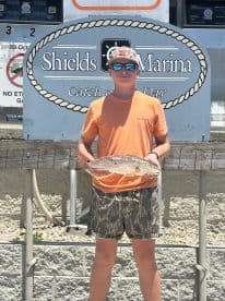Young angler proudly displaying a Redfish at Shields Marina after a successful fishing trip.