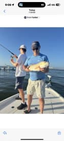 An adult angler proudly displaying a large fish while a young angler is actively fishing in the background, enjoying a day on the water.