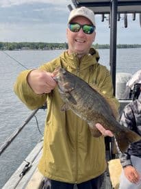 An angler proudly displaying a large Smallmouth Bass while fishing on a serene lake, showcasing a successful day on the water.