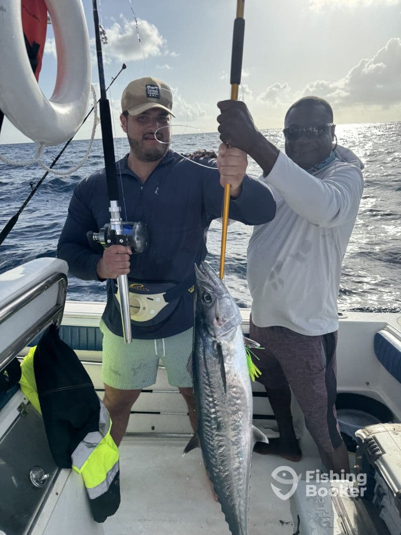 Two anglers proudly displaying a large Kingfish aboard a fishing boat, showcasing a successful deep-sea fishing trip.