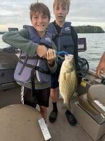 Two young anglers proudly displaying a large striped bass while fishing on a boat, showcasing a fun day on the water.