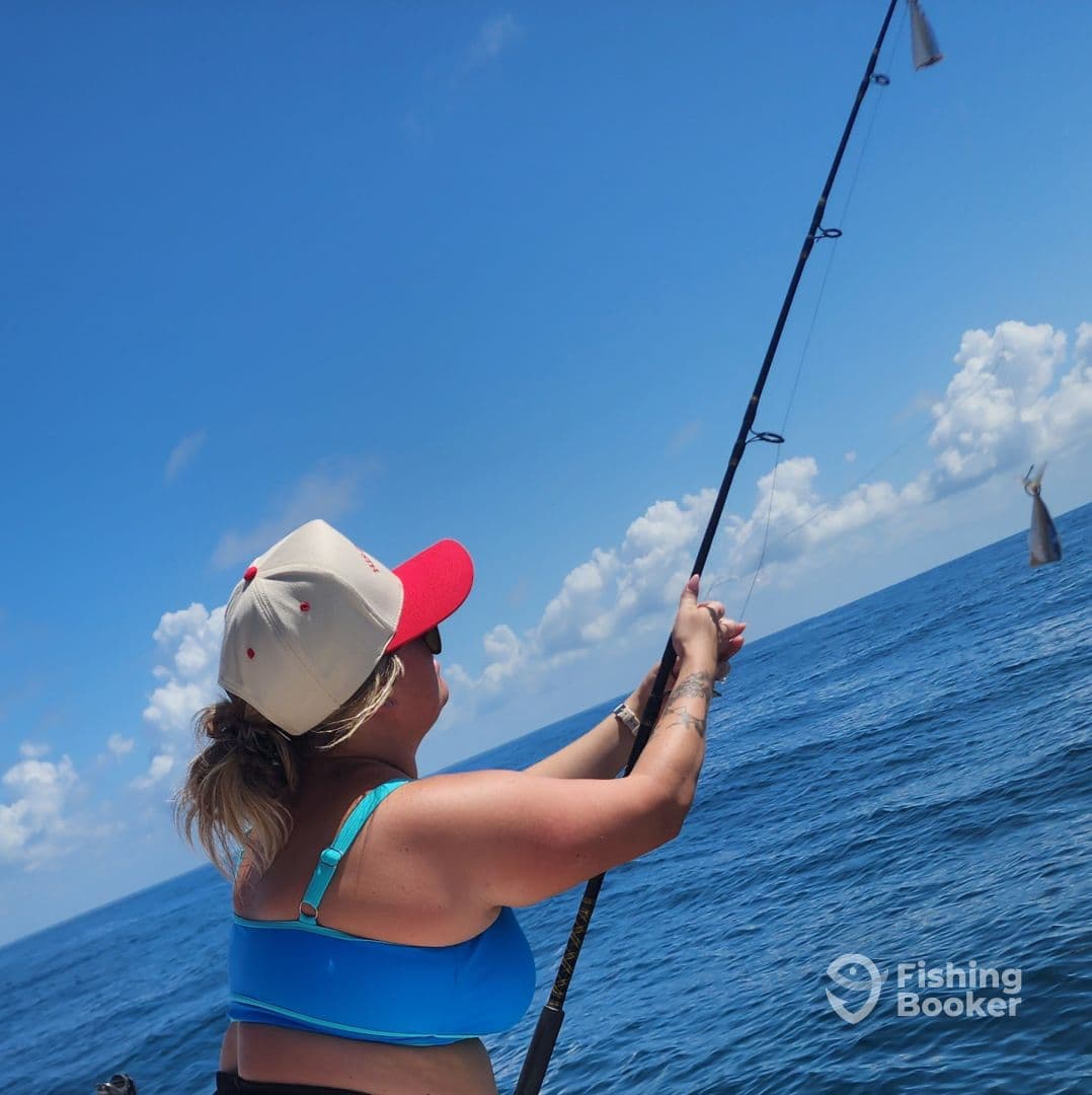 A woman actively reeling in a fish while fishing offshore, showcasing the excitement of a deep-sea fishing adventure.