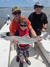 A young angler proudly displays a caught shark while enjoying a family fishing trip on a boat in coastal waters.