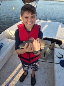 A young angler proudly displaying a caught fish while fishing on a boat, showcasing a fun day on the water.