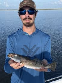 A young angler proudly displaying a Speckled Trout while fishing in a calm water environment.